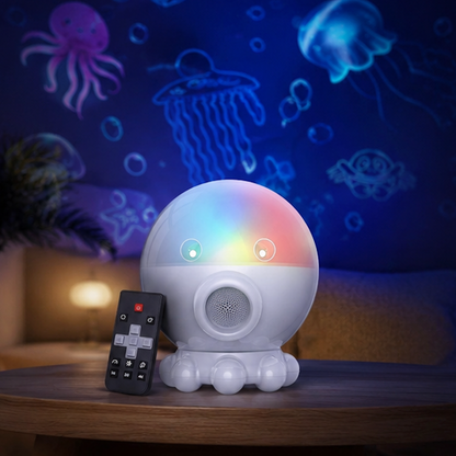 A white octopus-shaped light projector toy with colorful glowing eyes and a small black remote control, placed on a wooden table in a dimly lit room with blue jellyfish and sea-creature wall projections.