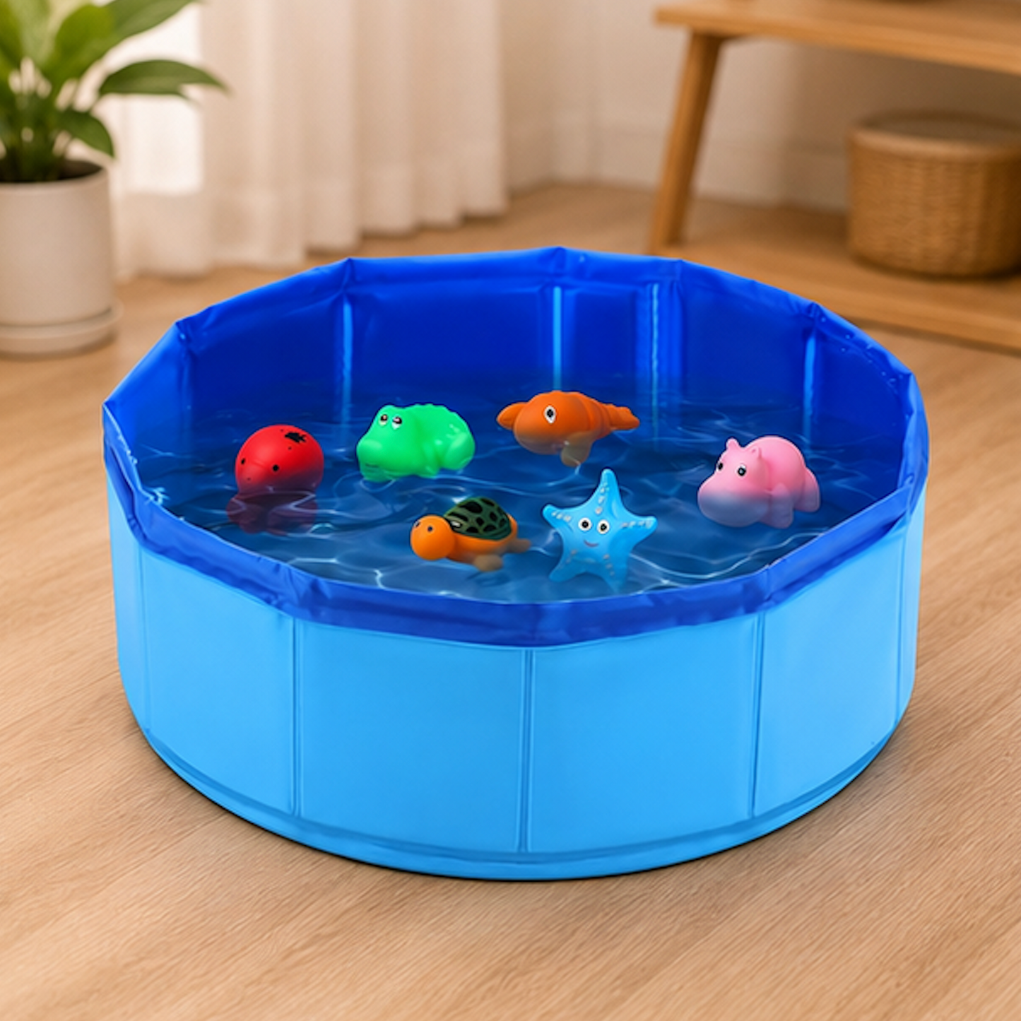 A blue collapsible plastic pool filled with water and several colorful floating bath toys, placed on a light wood floor in a home setting.