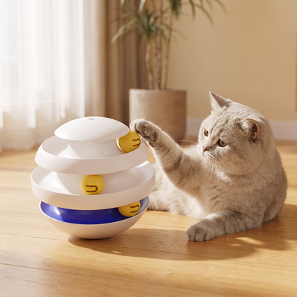 A light gray cat plays with the Wobble Orbit Ball Track Cat Toy on a wooden floor in a warm, sunlit room.