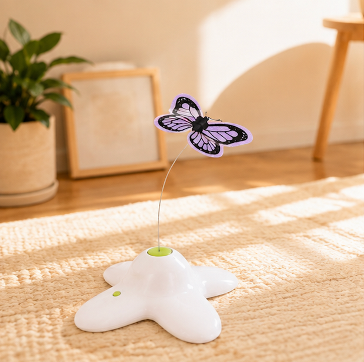 A white star-shaped Spinning Butterfly Cat Teaser base with a flexible wire holding a purple butterfly attachment, sitting on a beige woven rug in a sunny room with a potted plant and framed picture in the background.